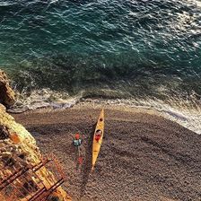 A kayak on calm blue coastal water seen from above.