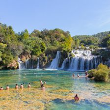 A waterfall surrounded by dense green vegetation with people swimming at its base.